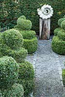 An ammonite sculpture by Darren Yeadon surrounded by box topiary, is set within yew hedges in a formal garden.
