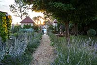 Gravel path lined with lavender and stachys leading to walled swimming pool and pavilions