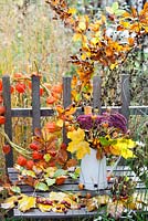 Autumn leaves and perennials in a jug - maple, Verbena, Rosehips, hornbeam, Sedum 'Herbstfreude', Verbena bonariensis. Physalis wreath.