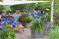 Women relaxing in garden with pots planted with Agapanthus and Liatris