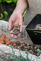 Practical step-by-step guide to planting a stone alpine trough with alpine plants. Alpine plants need good drainage, so cover the drainage holes first with crocks - to prevent them becoming blocked, and then cover with gravel to a depth of 2-3cm.