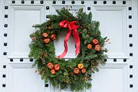 Lovely old front door is decorated with a  traditional, long lasting Christmas wreath made using spruce, with red rose hips, dried pumpkins and ribbon. 