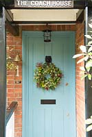 A cottage door decorated with a Christmas wreath made from evergreen foliage picked from the garden, mixed with holly and old man's beard. 