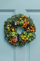 Festive wreath on blue front door.  Made of everlasting flowers, seedheads and chillies, wired and inserted through evergreen foliage and into wire frame. 