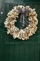Christmas wreath on dark green door. A 45cm circular frame of twigs provides a sturdy base onto which to glue delicate sprigs of honesty interspersed with bunches of sea holly - eryngium, sprayed silver and gold. 