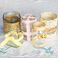 Decorating glass jars for garden posies step by step: A selection of glass jars decorated with gingham ribbon, gardener's jute twine string, cotton lace, rafia and dried rose buds.