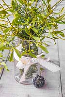Mistletoe placed in a glass jar with a ribbon, used as a table decoration. 