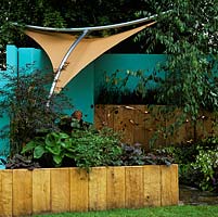 Buff coloured canvas awning suspended from stainless steel frame creates shade in a small, modern courtyard. Walls painted in blue create unusual backdrop.