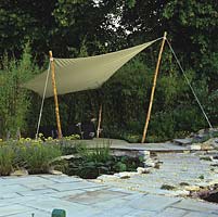 Sail awning on wooden poles by rustling bamboos enclose paved seating area by lily pond, edged in stepping stones set in chippings, paving, achillea, catmint and grasses.