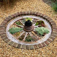 Set into gravel and edged in brick, a cartwheel with 14 segments filled with spring bulbs, succulents and alpine plants.
