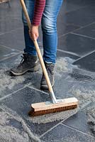 Brushing fast drying resin based mortar into the joints between black limestone paving stones with a broom.