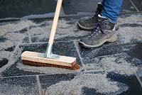 Brushing fast drying resin based mortar into the joints between black limestone paving stones with a broom.