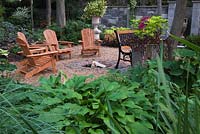 Hosta plants and wooden adirondack chairs next to a fire pit in backyard garden in summer, Jardin Secret garden, Quebec, Canada