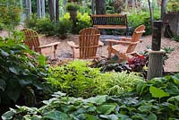 Hosta plants and wooden adirondack chairs next to fire pit in backyard garden in summer, Jardin Secret garden, Quebec, Canada