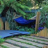 Shaded by tree fern, hammock hung above metal, egg crate flooring which abutts oak sleepers interplanted with chamomile and thyme - a low maintenance lawn alternative.