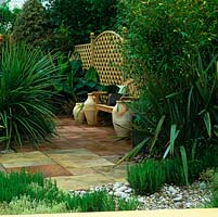 Paved courtyard with seat against wooden trellis by terracota urns. Bananas, bamboo, photinia, cordyline, phormium, rosemary and silver thyme planted around.