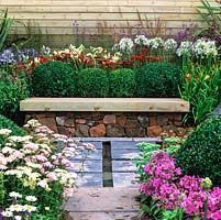 Sanctuary for escape and relaxation. Wood bench seat built on dry stone wall, backed by box balls, achillea, daylily, penstemon, agapanthus. Box balls double as back to bench in small space.
