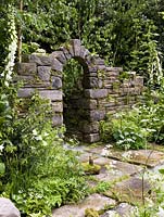 Natural stone arch in folly set in woodland. Native ferns and mosses fill fissures in wall, whilst foxgloves and cow parsley reach for light.