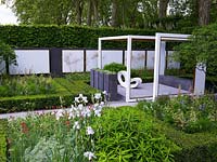 Pergola-like wooden frames focus attention on views within the space. Geometric layout of box and hornbeam mixes with perennials and shrubs. Raised patio with chair.