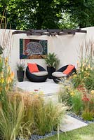 A contemporary courtyard garden with seating area, surrounded with Stipa and Calamagrostis grasses with Achillea, Kniphofia and Eryngium.