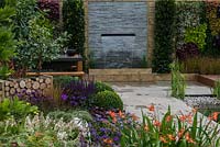 An outdoor room with dining table, stone water feature and pond with vertical planting.