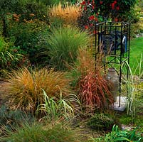 Stained glass obelisk by red-leaved Miscanthus sinensis. On left, clump of rusty Stipa arundinacea. Pennisetum alopecuroides. and Panicum virgatum Warrior.