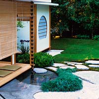 Verandah looks onto idealised natural Japanese landscape of dry stream, shallow pool fed by rain chain from roof, rock placings, stepping stone path and woodland.