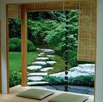 Seen from verandah, idealised natural Japanese landscape of dry stream, shallow pool fed by rain chain from roof, rocks, stepping stone path and woodland.