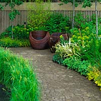 Calm retreat with curving chairs on courtyard edged in different shades of green from bamboo, euphorbia, alchemilla, grasses and rheum.