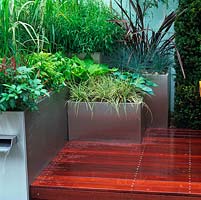 Urban courtyard retreat, with modern steel planters, smooth decking, oak table and seat, stainless steel planters with tranquil planting to add height, splashing waterfall and rill.