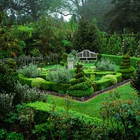 Herb garden contained within low box hedges, and defined by topiary. Sundial. Overlooked by Lutyens style bench. Palms and phormium create backdrop.