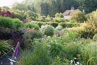 View across grasses, hardy geraniums and euphorbias to a thatched cottage outside the garden, characteristic of this part of Dorset. Littlebredy Walled Gardens, Littlebredy, Dorset