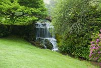 The River Bride tumbling down a cascade as it leaves the lake in the grounds of Bridehead House. Littlebredy Walled Gardens, Littlebredy, Dorset