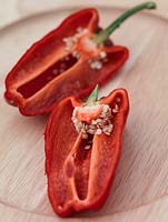 Chilli 'Apache', a red chilli sliced lengthways to show the seeds, on a wooden plate.