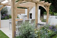 Seating area under pergola with BBQ and outdoor woodburner, Olearia x haastii in a border with Echinacea 'White Swan', Achillea 'Walther Funcke', Carex testacea, Nepeta 'Walkers Low' and Orlaya grandiflora, Al Fresco, RHS Hampton Court Palace Flower Show 2014 