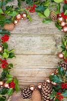Wooden surface with a border of Copper baubles, Pine cones and Ilex aquifolium foliage.