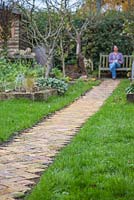 Woman sat on a garden bench at the end of the new brick path. 