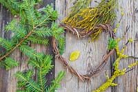 A grapevine heart on a wooden surface, accompanied with Yew foliage, Prunus with Lichen and Conifer foliage