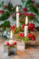 Candles mounted in metal star cutters, with moss and Ilex aquifolium berries