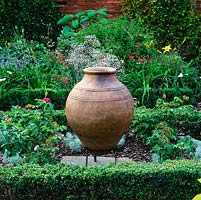 Box-edged bed is filled with Rosa 'De Rescht', a huge old terracotta urn at its centre.