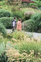 Visitors to large urban public park designed by Peter Kluska. Mixed perennial planting dominated by grasses and laid out in a naturalistic style by Rosemarie Weisse. Westpark, Munich, Germany.
