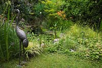 Metal Heron bird sculptures next to pond in backyard garden in summer, Quebec, Canada