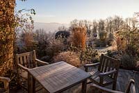 Terrace with teak chairs and table overlooking borders with perennials, grasses and shrubs - December, Mas de Bety, France