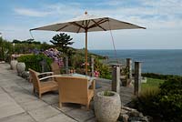 Coastal garden with Hydrangeas, Agapanthus, stone pots, chairs, a parasol with a view to the sea. The Lizard, Cornwall in August