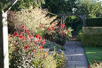 Path through decorative wooden archway with autumn planting including Dahlia 'Bishop of Llandaff', Stipa gigantea and Fennel 