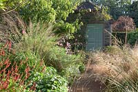 Gravel path to decorative wooden hut with autumn borders including Geraniums, Persicaria amplexicaulis, Grasses and Verbena bonariensis