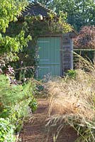 Gravel path to decorative wooden hut with autumn borders including Grasses, Verbena bonariensis, Ricinus communis