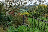 A view of a statue surrounded by Euphorbia mellifera, fennel and Rosa Hertfordshire. Beyond,  a rill leads the eye to the view of Axe Valley.