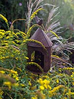 A small metal bird feeder surrounded by Solidago 'Fireworks' and Miscanthus grass.