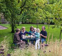 Family having tea and cake in the cool of the orchard.
